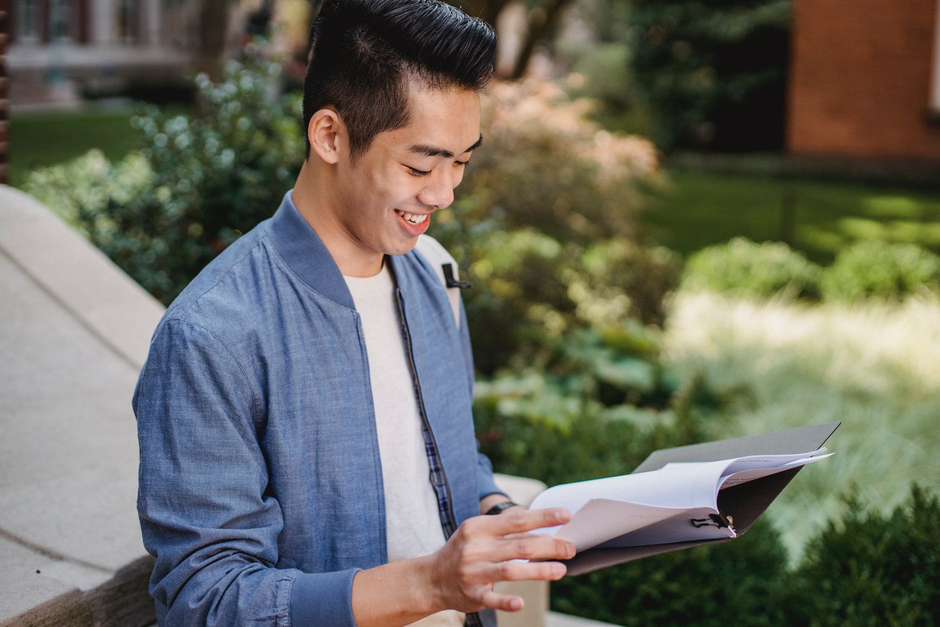 smiling ethnic student reading document in park